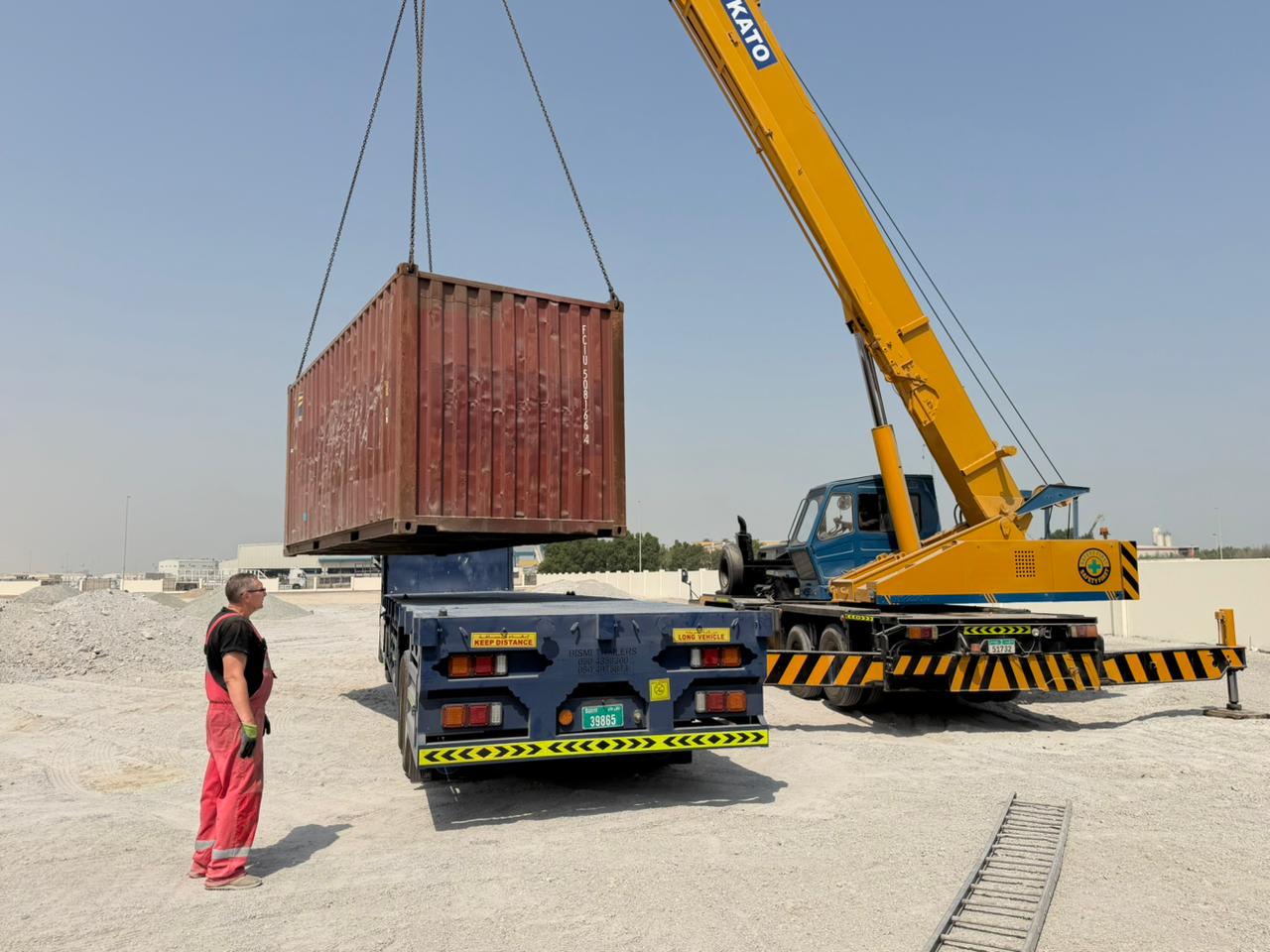 Crane lifting a shipping container onto a delivery trailer at a UAE site
